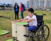 ילד יושב בכיסא גלגלים ומנגן בתופים בגן ציבורי