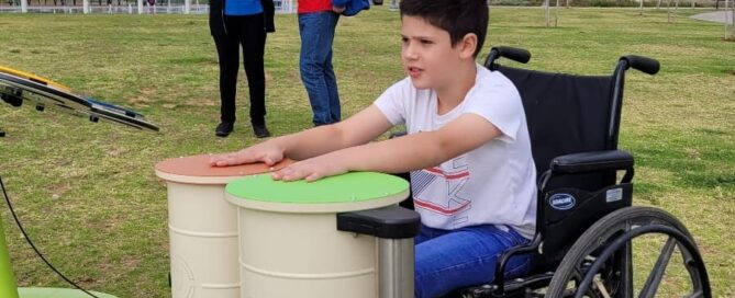 ילד יושב בכיסא גלגלים ומנגן בתופים בגן ציבורי